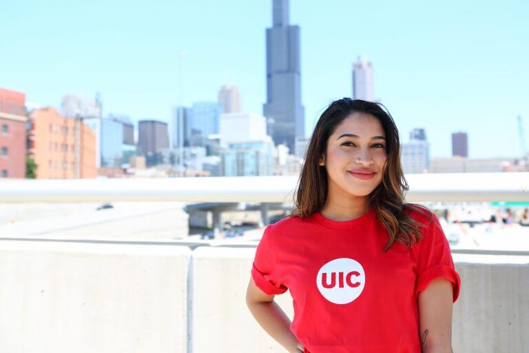 Smiling Hispanic female with red and white UIC-logo t-shirt in front of Chicago skyline