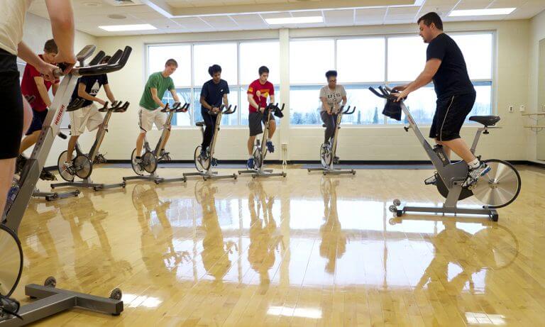 spinning class being led by male instructor in sunny gym