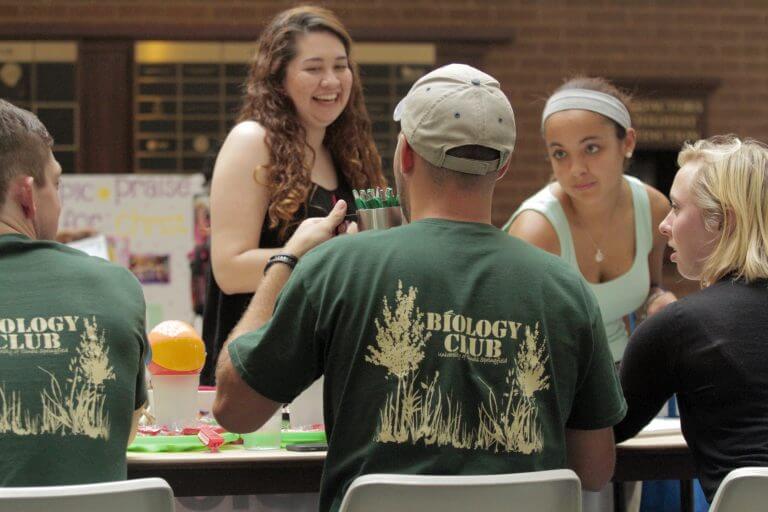 students at table laughing and talking wearing Biology Club t-shirts