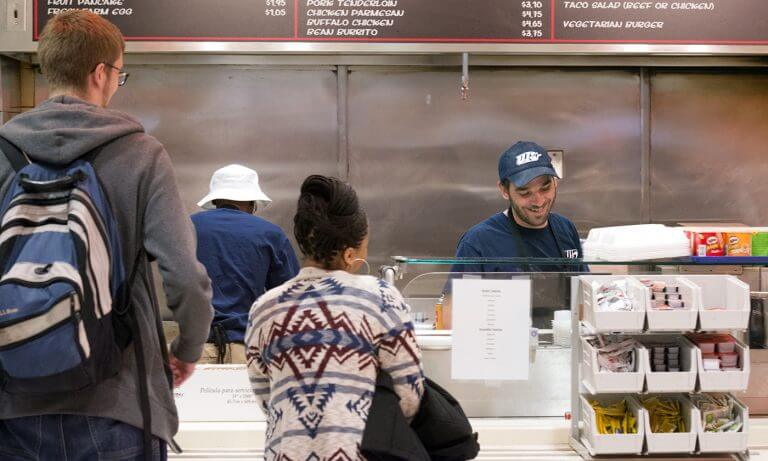 students in line to get food from smiling worker in uniform at dining hall
