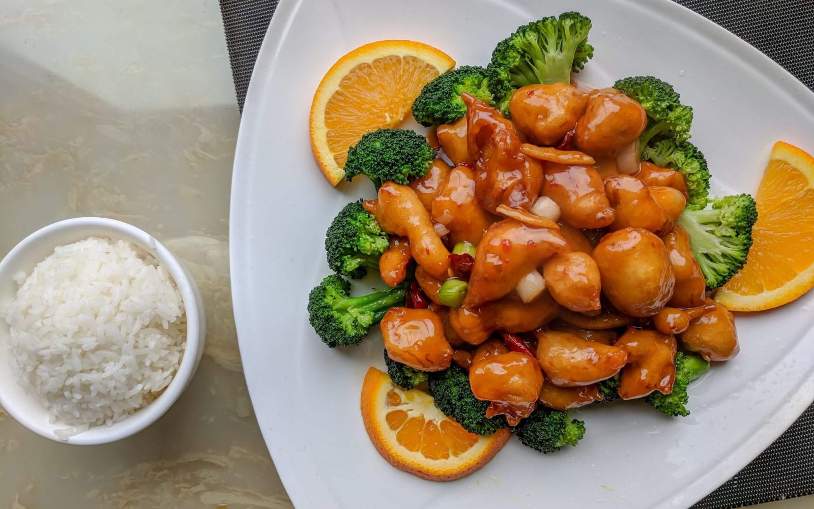 bowl of rice and plate of Asian chicken and broccoli dish with orange slices