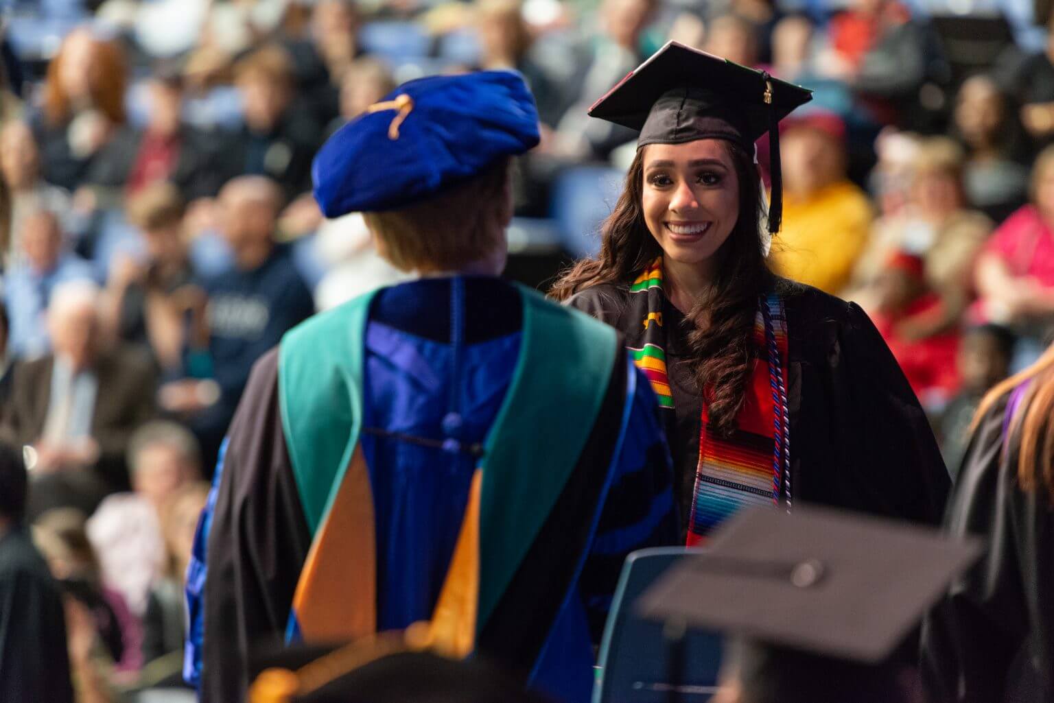 Female graduate in cap and gown crossing stage and receiving diploma