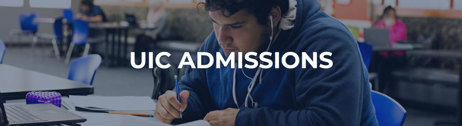 male student wearing earbuds at desk in class doing work with paper and pen