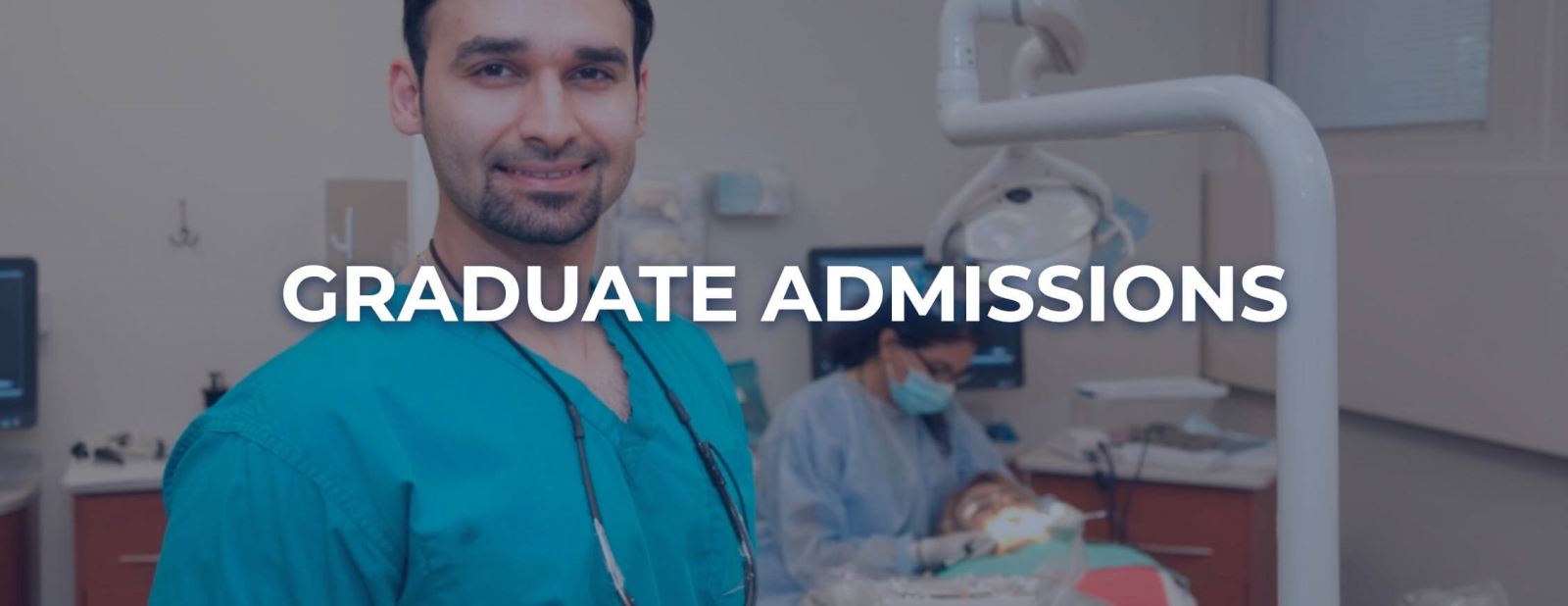 Male in surgical scrubs with beard smiling while dental patient being worked on in background